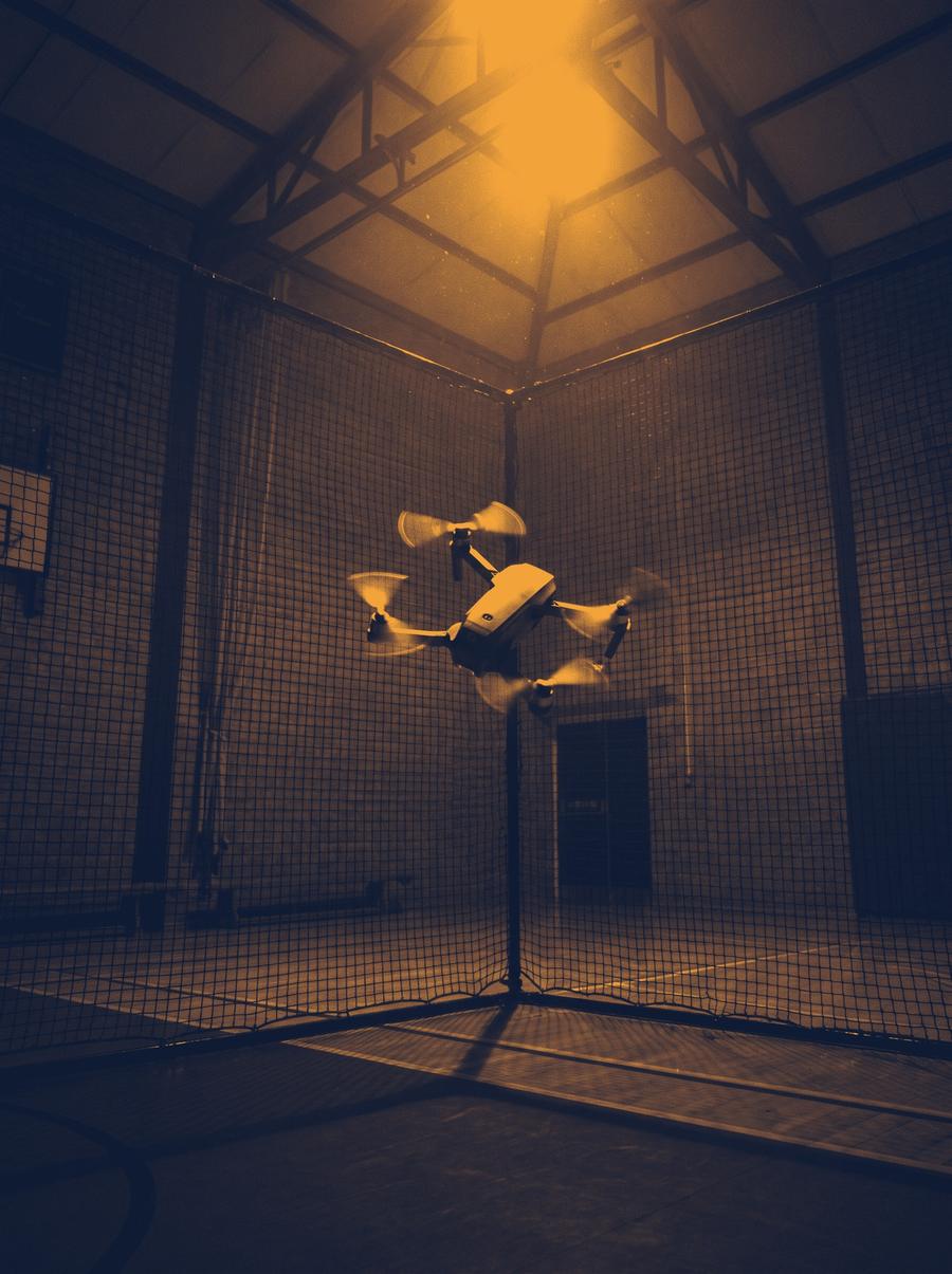 A small drone flying inside a netted safety cage