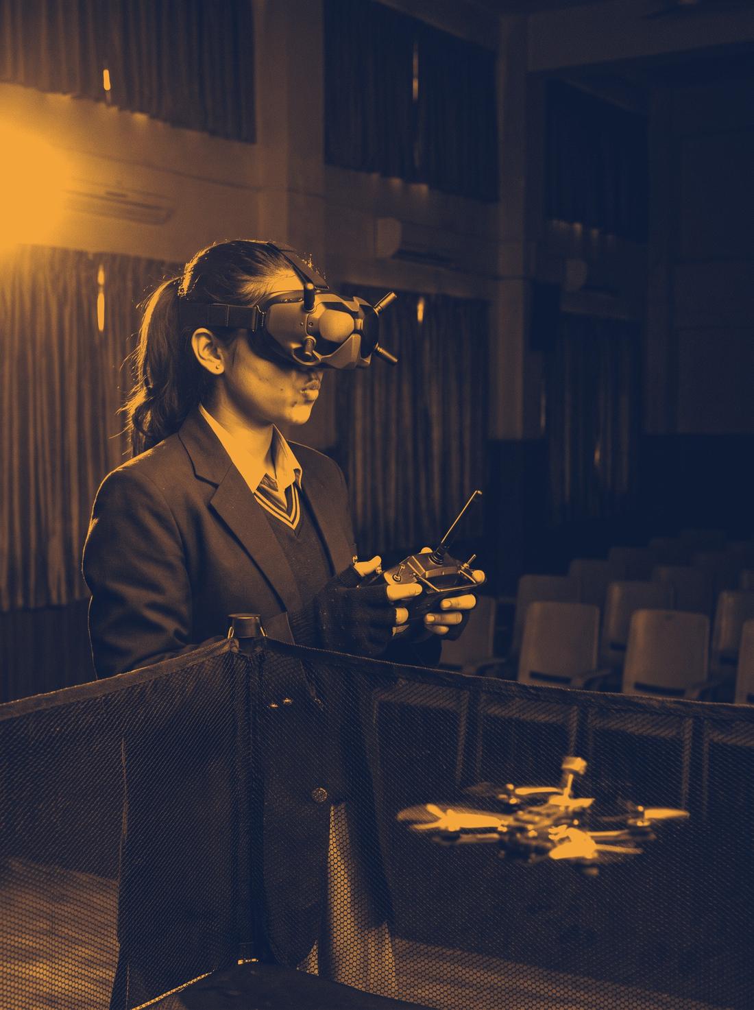 A student in FPV goggles flying a drone in the school hall