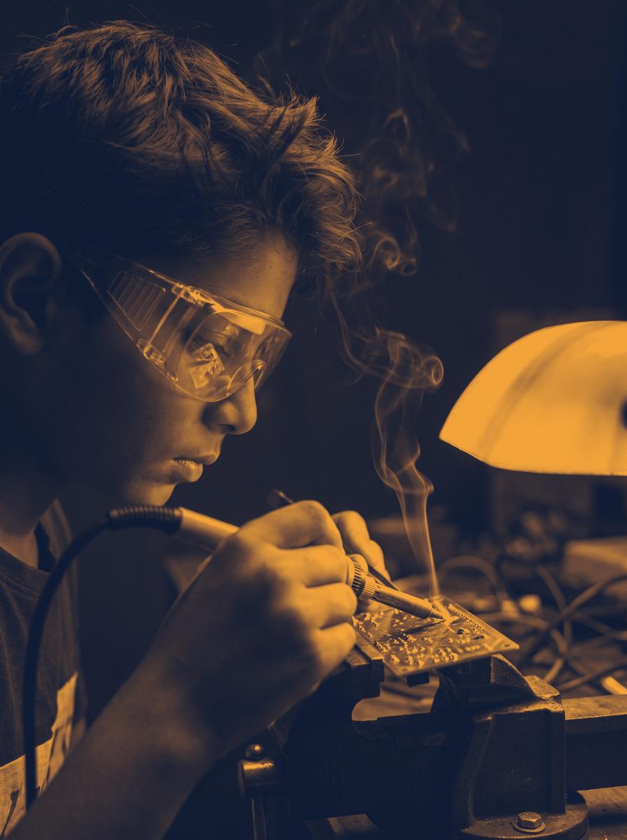 A boy in safety goggles soldering a circuit board
